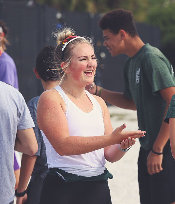 sarasota-scullers-club-0132631 Female rower in foreground speaking with someone off frame. Male rowers in background speaking to one another.